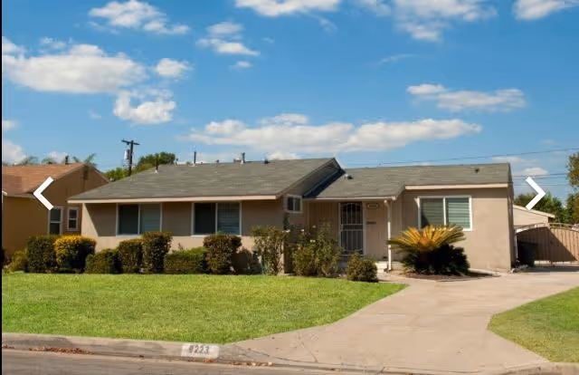 A single-story beige senior living facility with a manicured lawn and shrubs along the front.