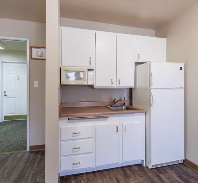 Compact kitchenette with white cabinets, laminate countertop, sink, microwave, and refrigerator.