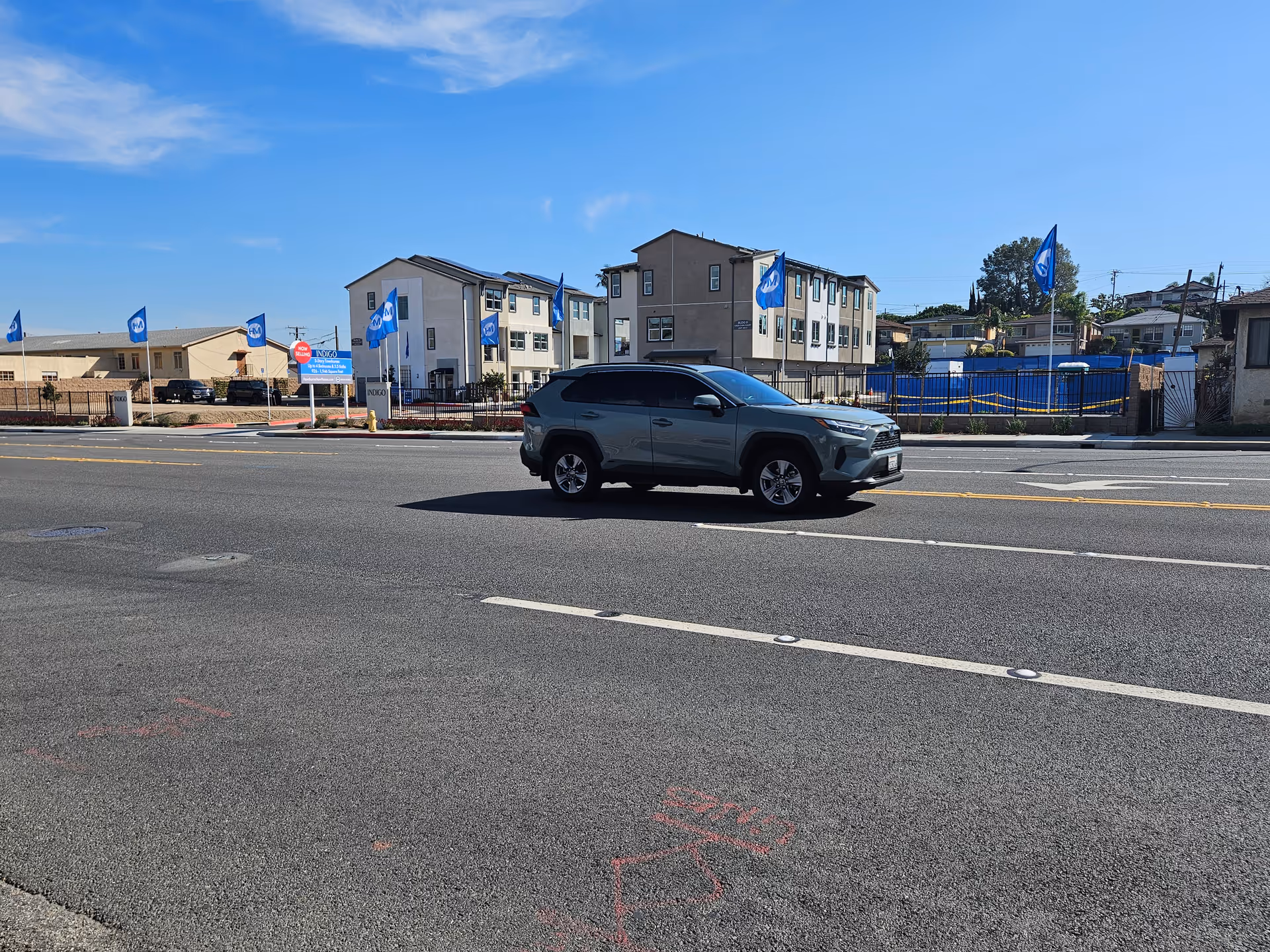 Gray SUV driving past a senior living facility exterior with blue flags and a fence.