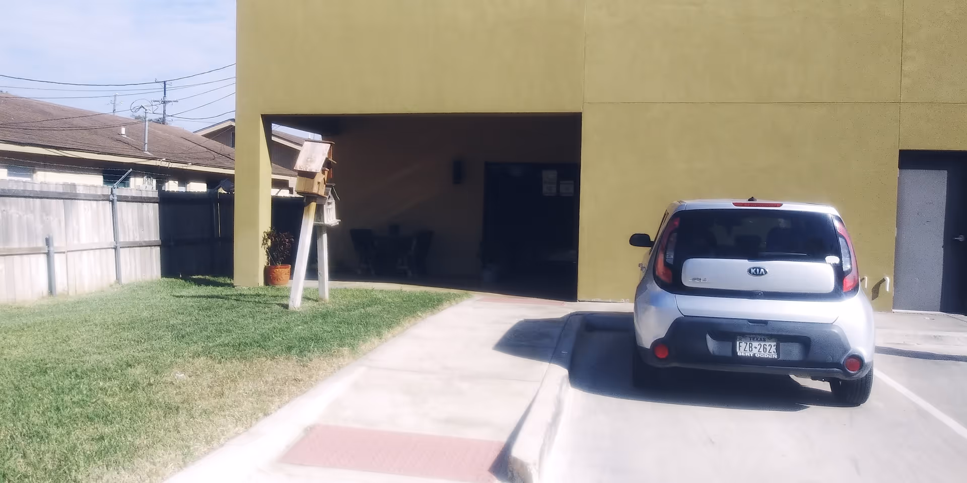 Exterior view of a greenish building with a driveway, parked car, and grassy lawn.