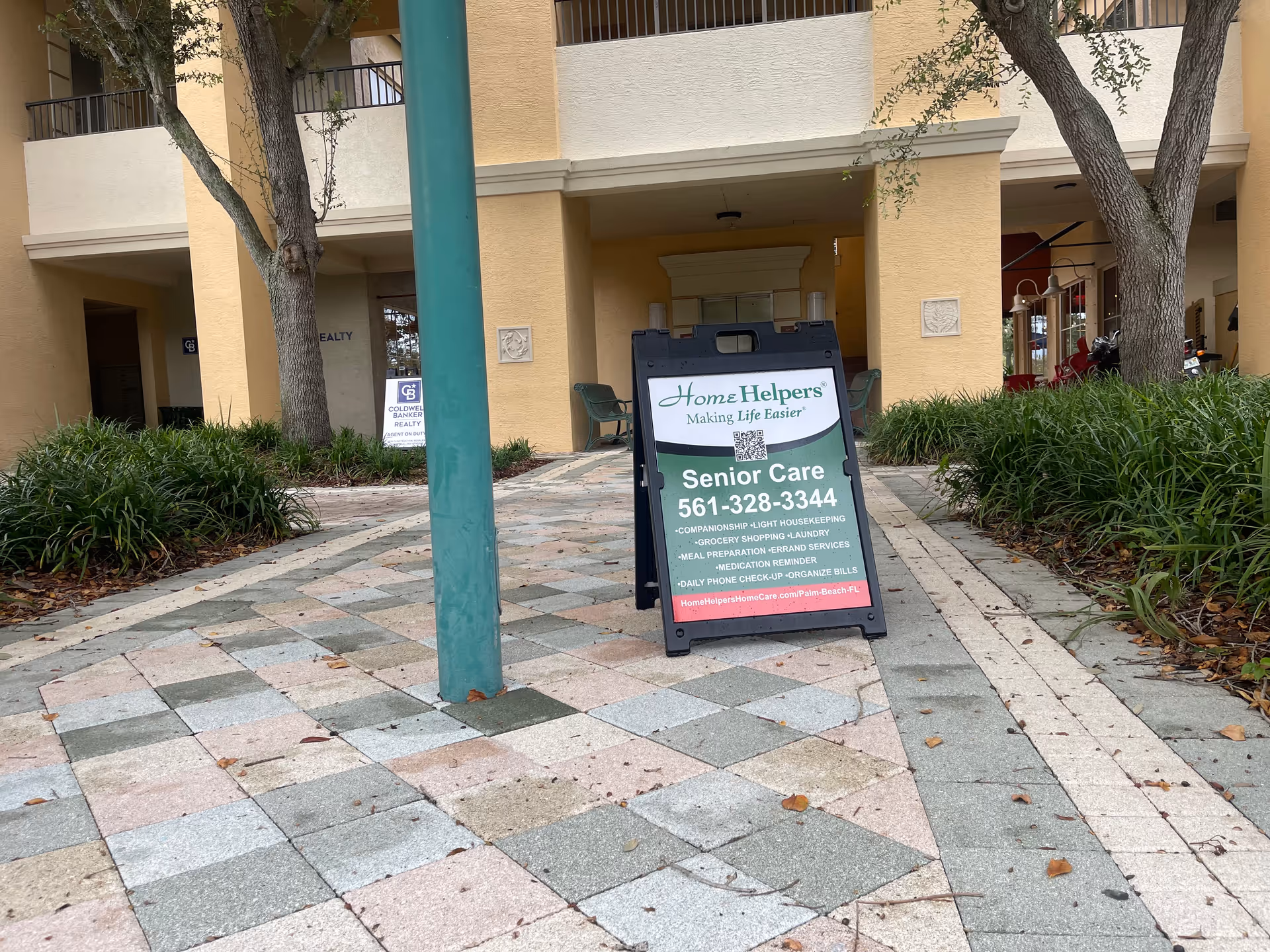 Outdoor view of a beige building entrance with a Home Helpers signboard on a striped walkway