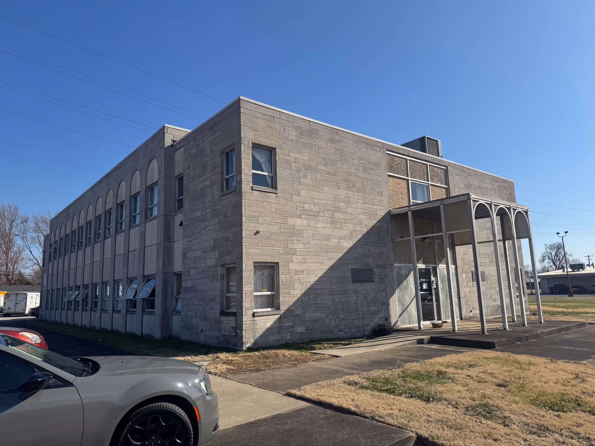 Exterior view of a gray stone senior living facility with arched windows and entrance.