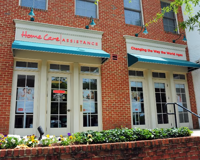 Exterior of Home Care Assistance Williamsburg building with brick facade, teal awnings, and flower bed.