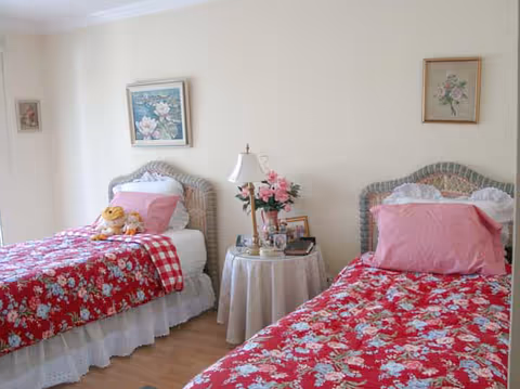 Two twin beds with pink floral quilts frame a shared bright bedroom with a nightstand.