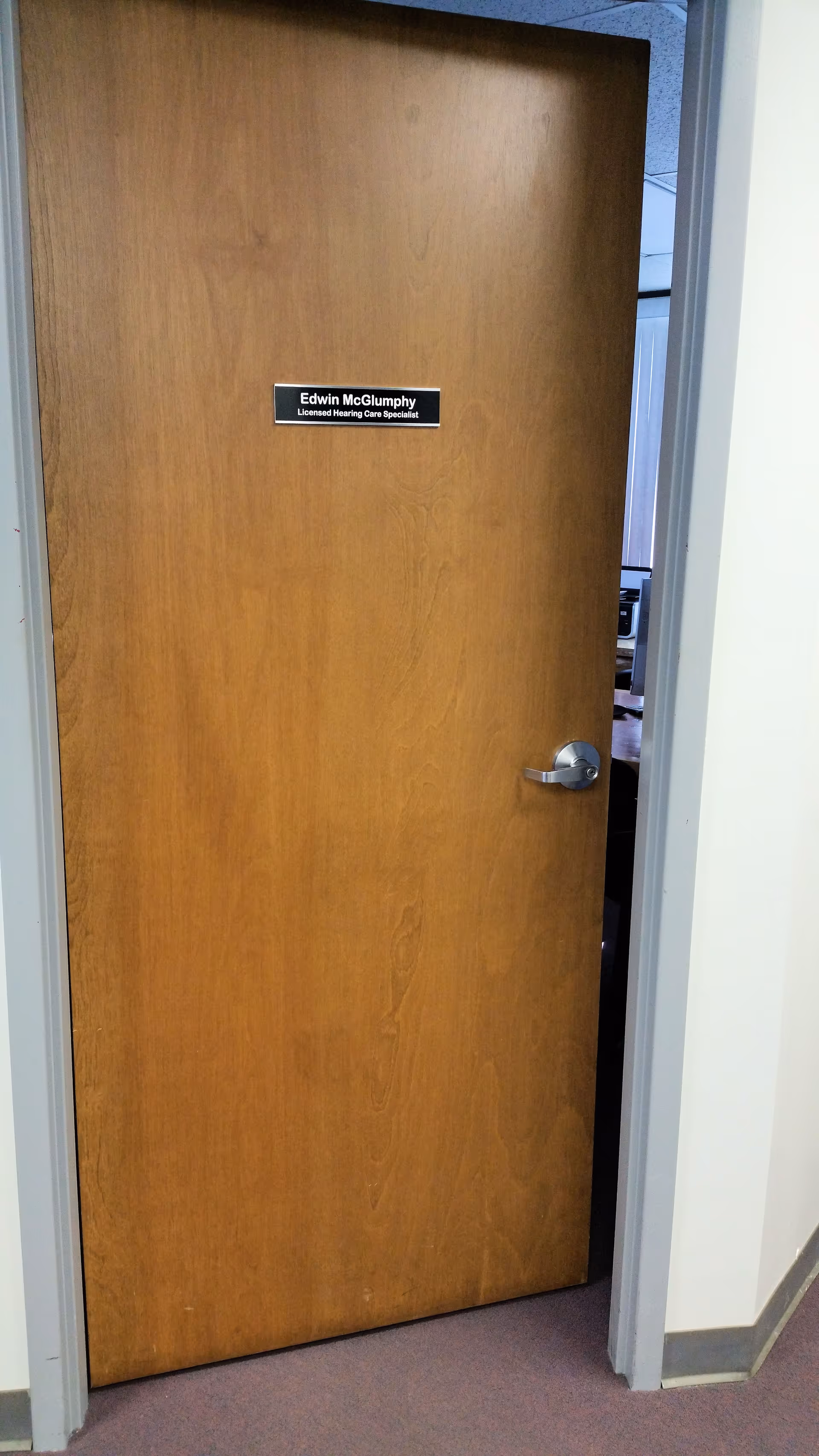 Wooden interior door with placard reading Edwin McGlumphny, Licensed Hearing Care Specialist.