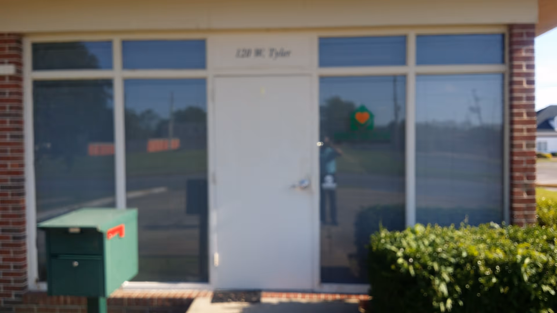 Front of a care facility with large glass windows, a central white door, and a green mailbox.
