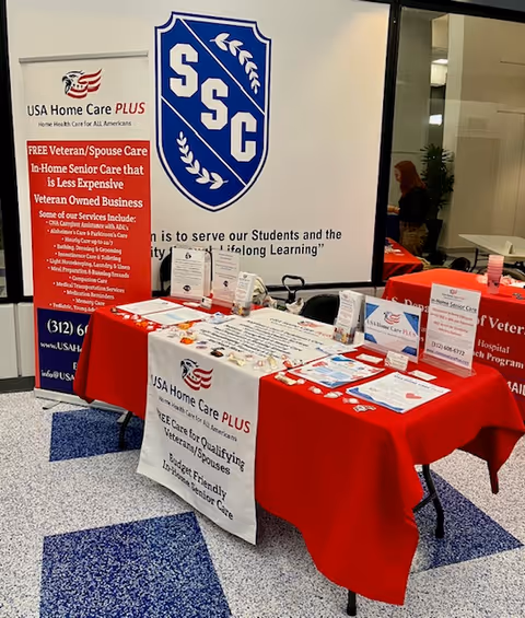 Indoor promotional display with tables, red tablecloths, and USA Home Care PLUS banners.