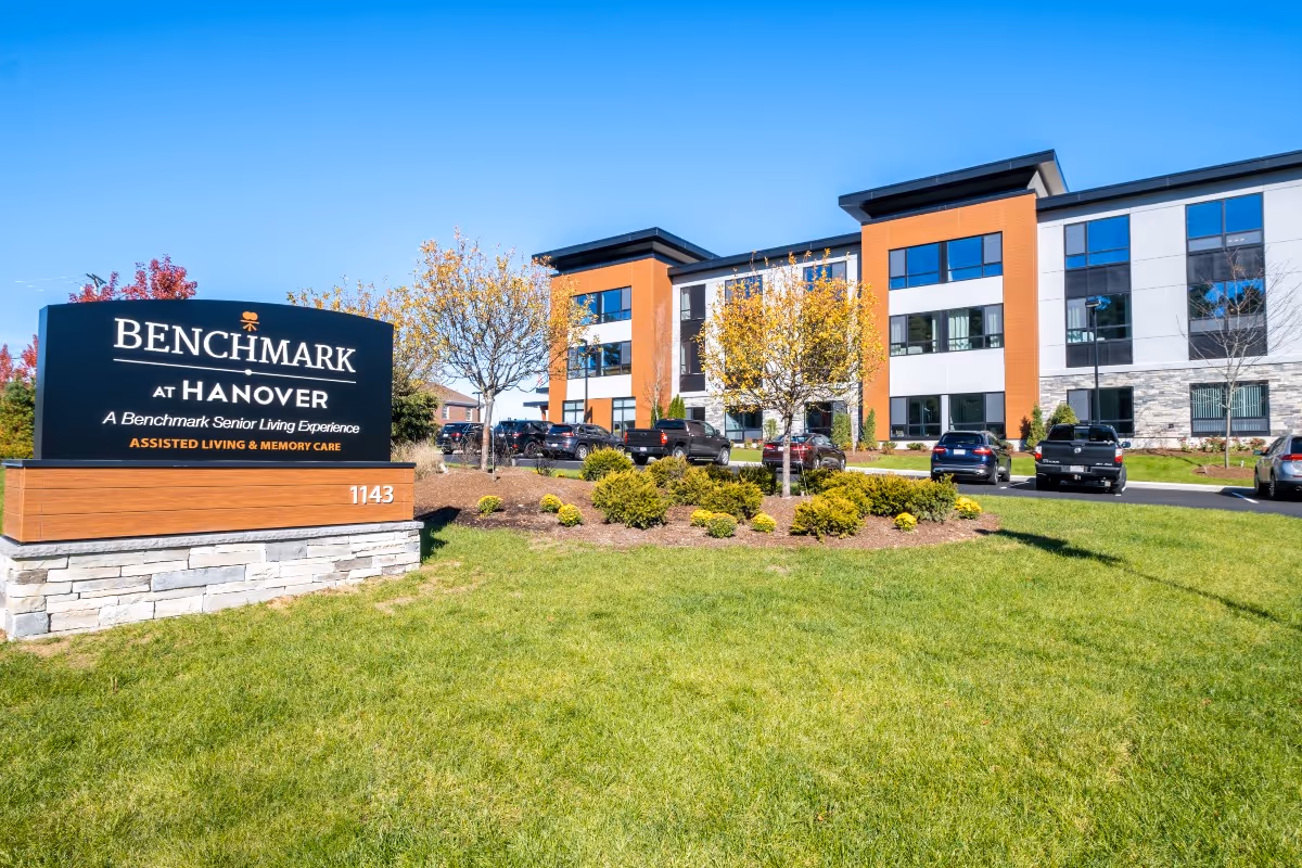 Exterior view of Benchmark at Hanover senior living facility with sign and parked cars