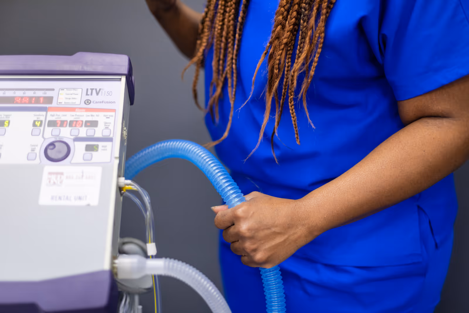 Caregiver in blue scrubs operates a medical device with a blue hose.