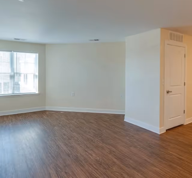 Bright empty living room with wood flooring, a window, and a doorway.