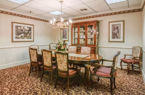 A formal, carpeted dining room with a wooden table, upholstered chairs, chandelier, and china cabinet.