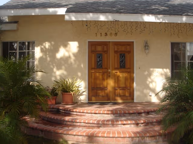 Front entrance of Charnock East with double wooden doors, brick steps, and potted greenery.