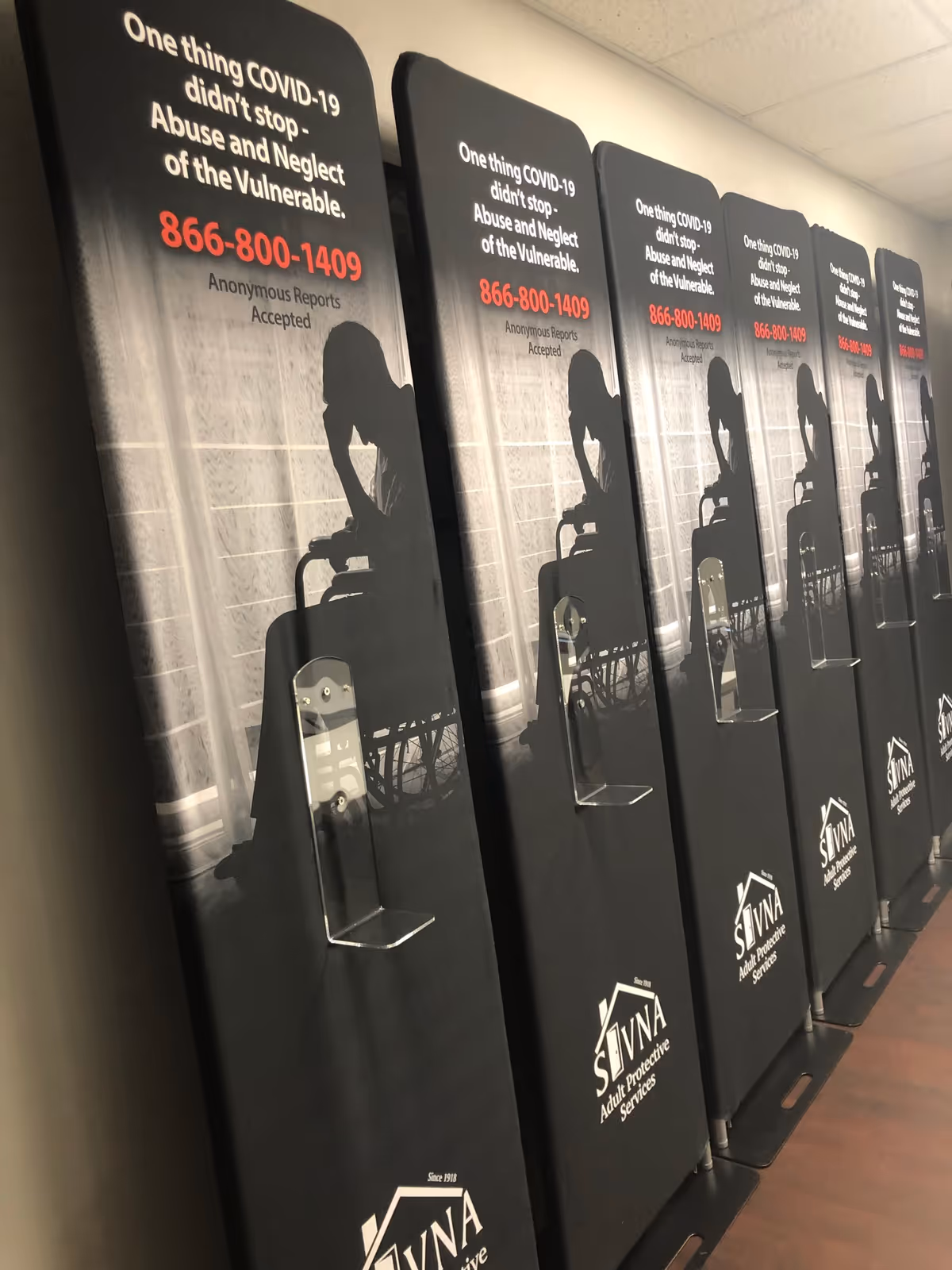 Indoor hallway lined with tall banners promoting COVID-19 abuse reporting hotline.