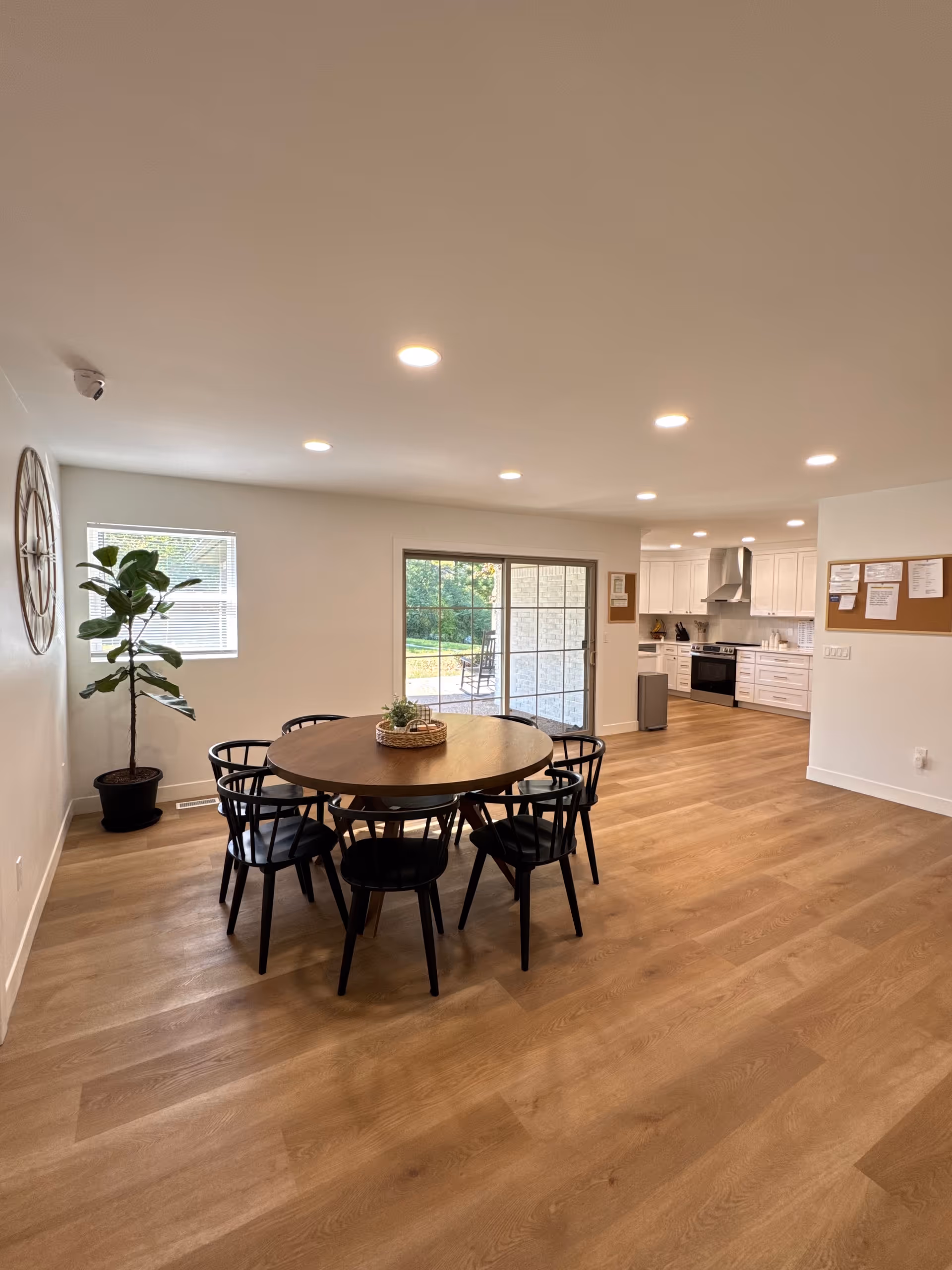 Round wooden dining table with eight black chairs in a bright open dining area.