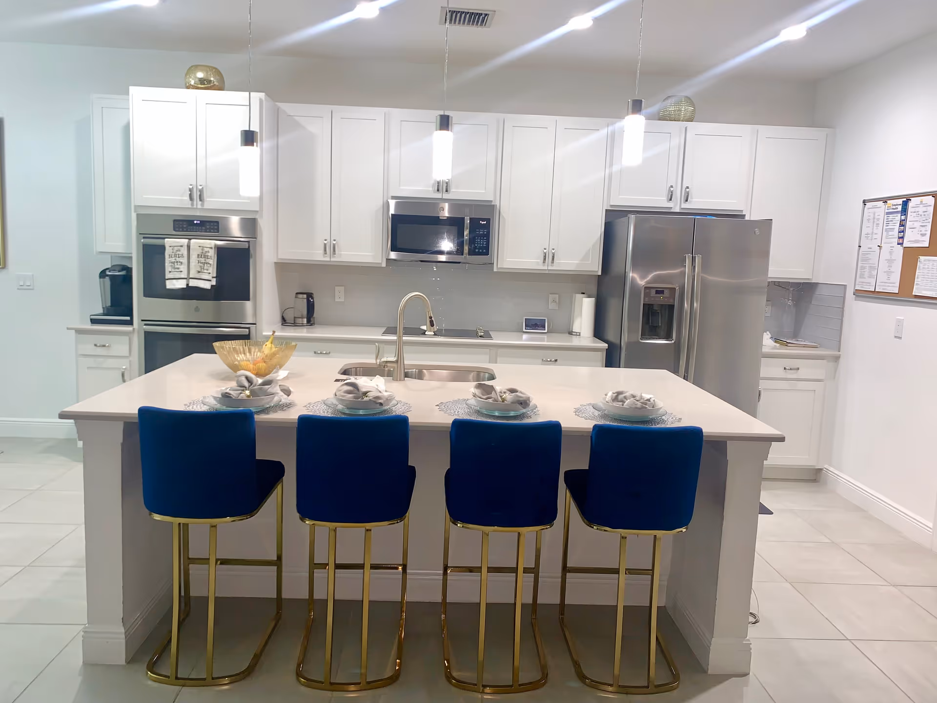 Modern white kitchen with island, four blue stools, and stainless appliances.
