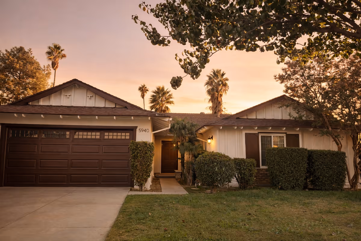 Single-story residential building with a two-car garage, front yard, and shrubs at sunset