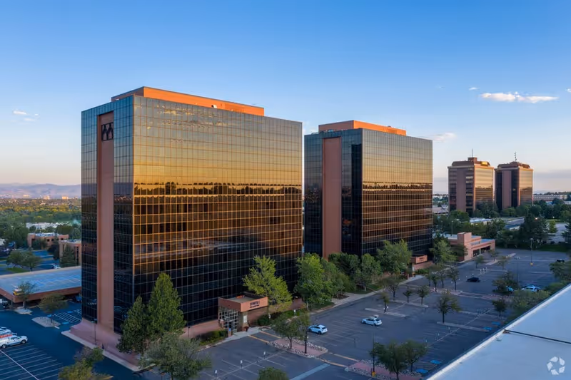 Aerial view of tall glass office buildings reflecting sunlight beside a parking lot.