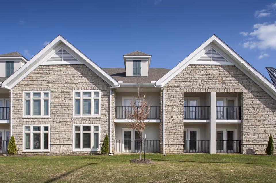 Stone-clad senior living building with twin gabled roofs and balconies