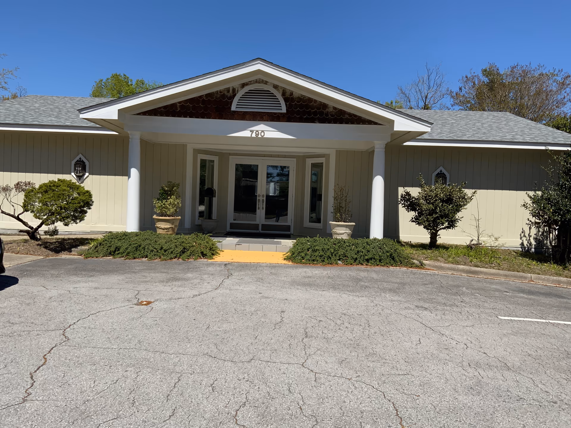 Exterior view of a single-story senior care facility entrance with columns and glass doors.