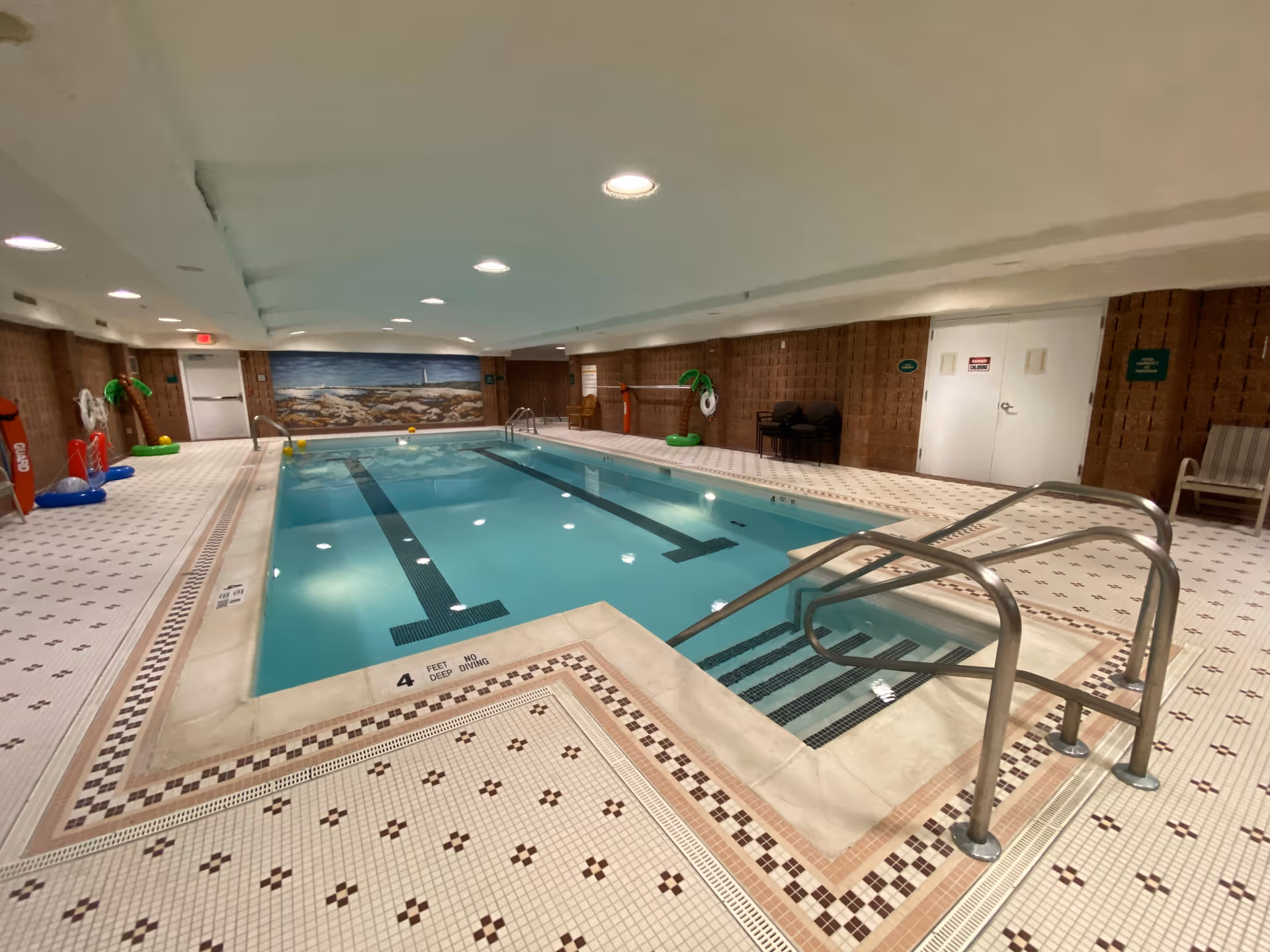 Indoor pool area with steps, metal railings, and a tiled deck surrounding the water.