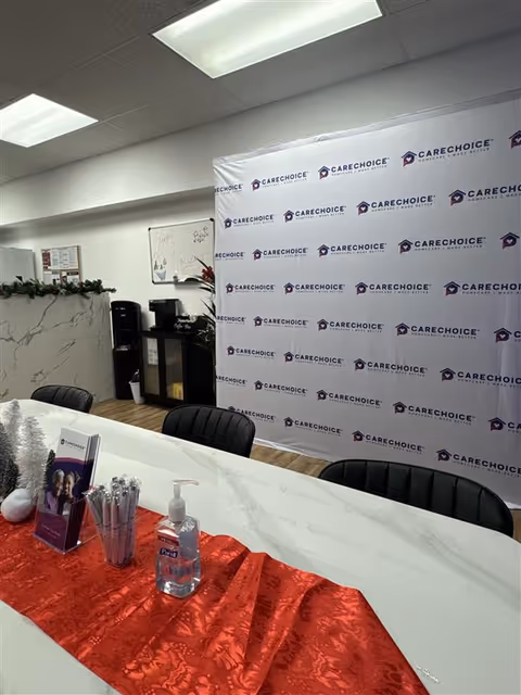 Indoor reception area with a branded CareChoice backdrop, long table, chairs, and hand sanitizer.