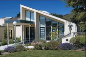 Modern senior living facility exterior with large glass front, entry steps, and landscaped grounds.
