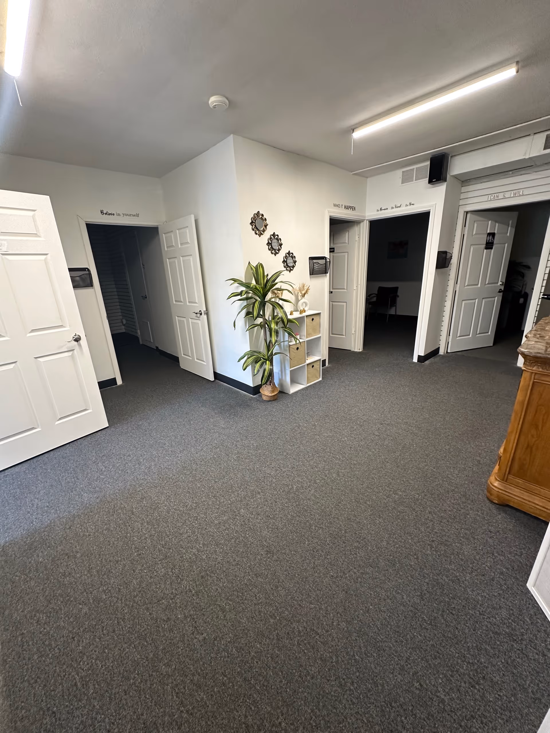 Indoor hallway in a senior living facility with multiple doors, a plant, and a small shelf.