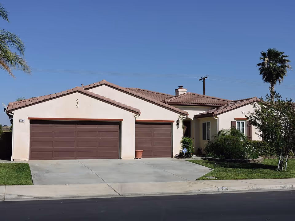 Single-story house exterior with two brown garage doors and a manicured front yard.