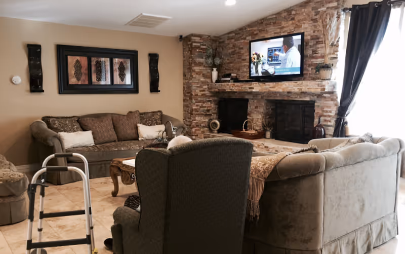 Cozy senior living room with sofa, armchairs, fireplace, and mounted TV.