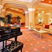Elegant hotel-style lobby with grand piano, plush seating, arches, and warm lighting.