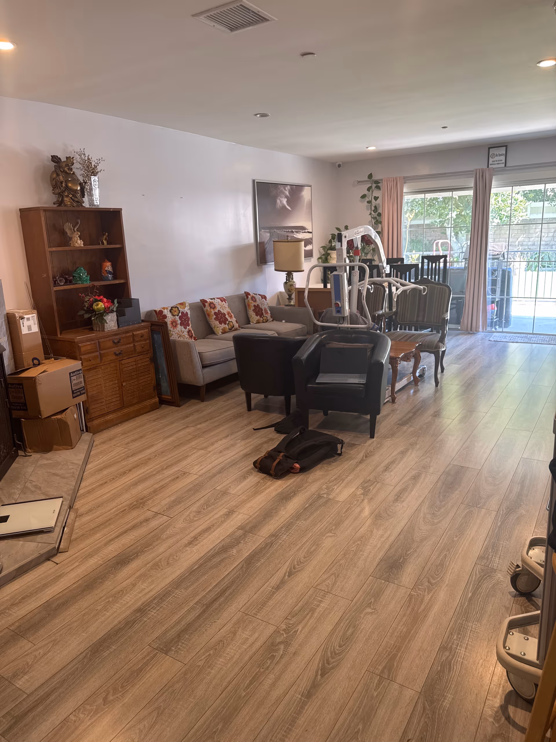 Cozy senior living lounge with sofa, chairs, and a wooden cabinet near a sliding glass door.