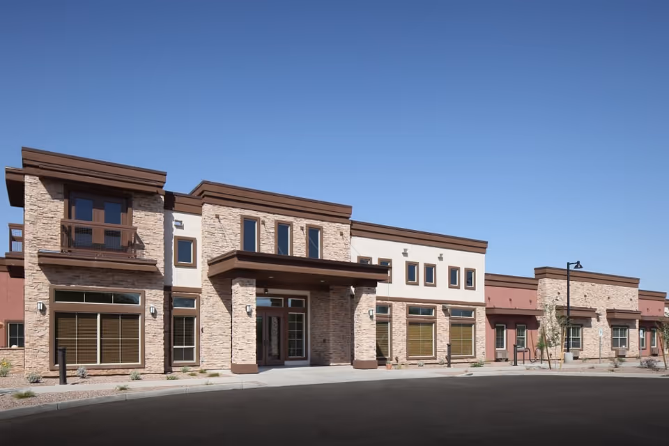 Front exterior of a modern stone-and-stucco senior living building under a clear blue sky.