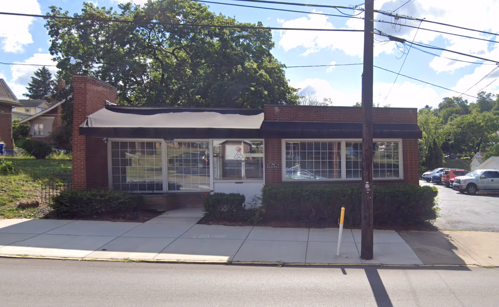 Brick one-story building with large glass windows and a sidewalk along the street.