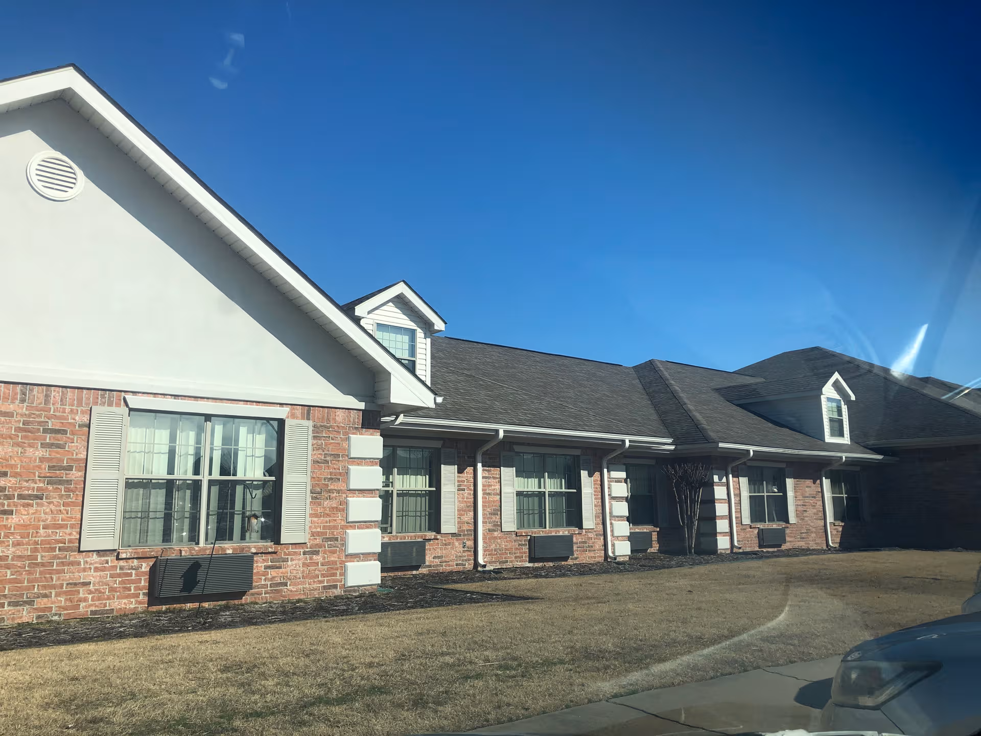 Exterior view of a brick senior living facility with a gabled roof and parked car.