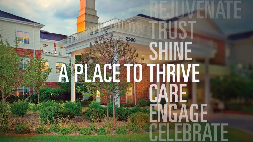Exterior view of Belmont Village Senior Living Glenview building with landscaped greenery and trees in front. The building has white and red brick walls, multiple windows, and a covered entrance with the number 2200 displayed. Words overlay the image including 'A PLACE TO THRIVE' and other motivational words like 'REJUVENATE', 'TRUST', 'SHINE', 'CARE', 'ENGAGE', and 'CELEBRATE'.