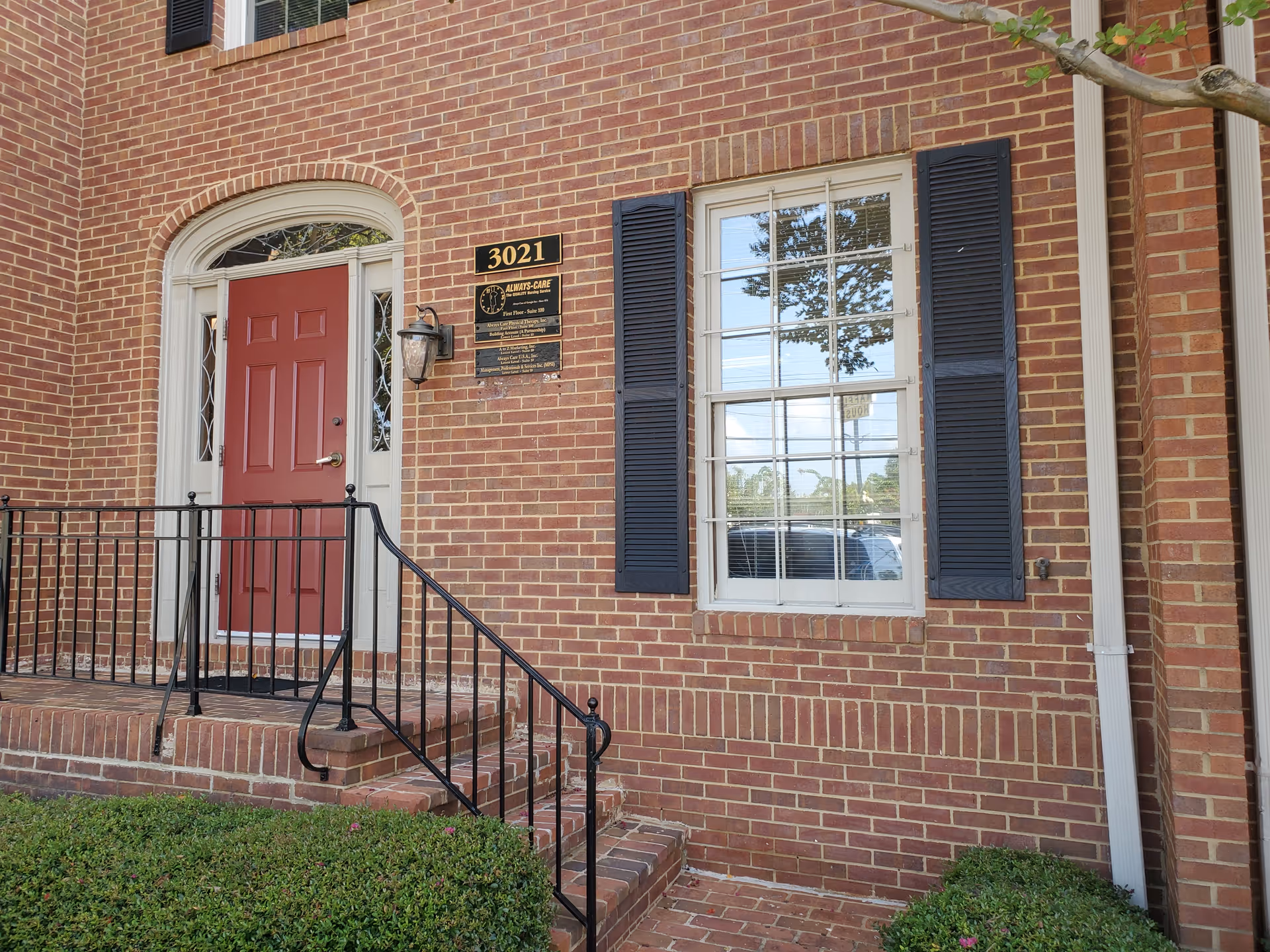Brick front entrance with red door, stairs, railing, and a window.