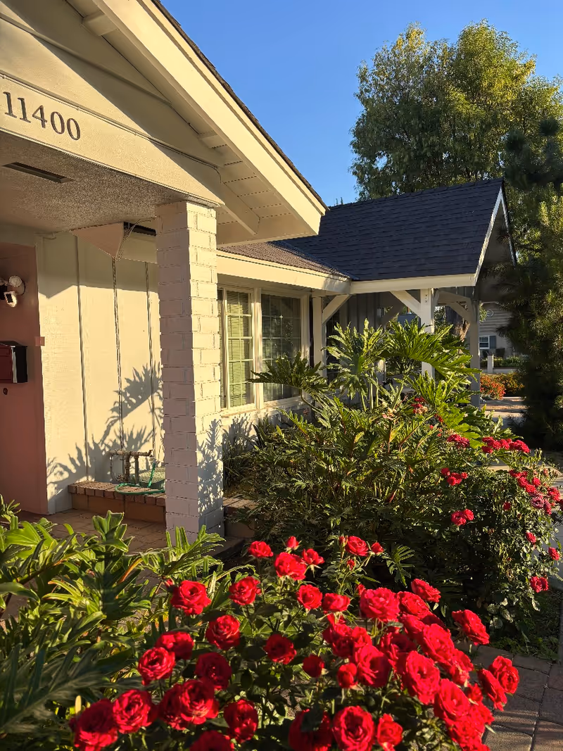 Exterior view of a senior living facility entrance with blooming red roses and landscaping.