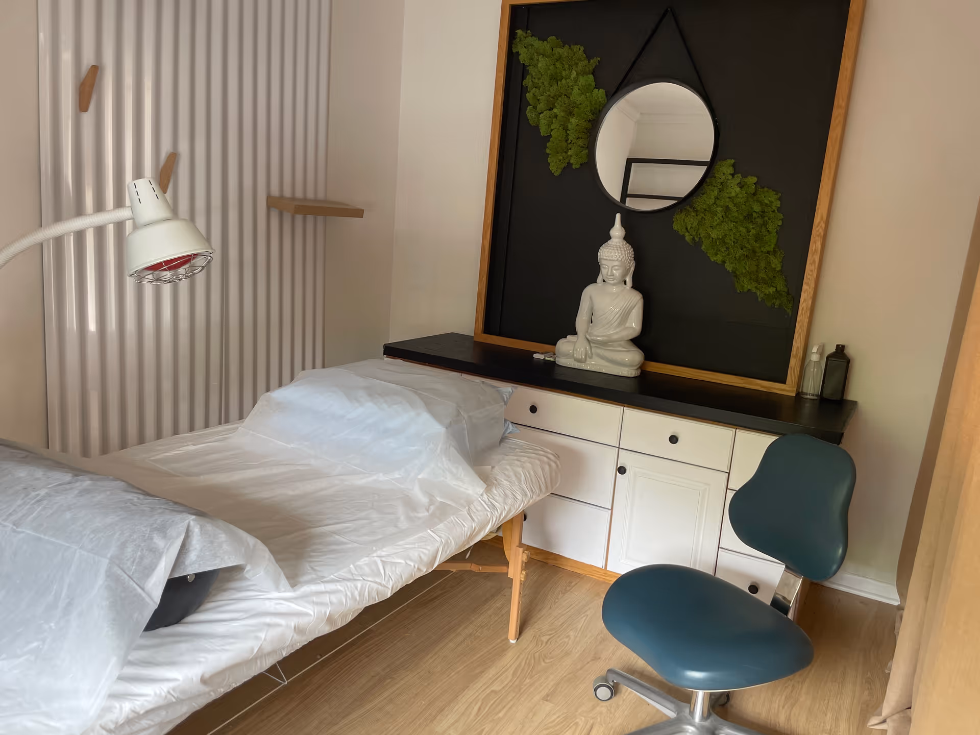 A treatment room with a covered single bed, desk, and Buddha statue centerpiece.