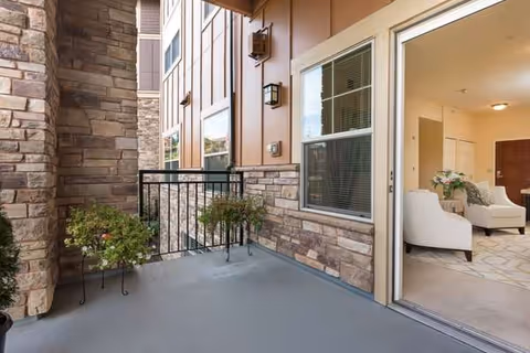 Outdoor balcony with potted plants, opening into a living room with white furniture