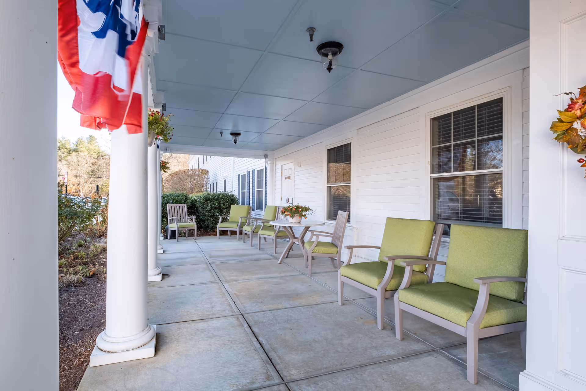 Covered outdoor porch with white columns, seating, and a flag.