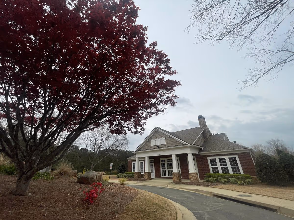 Front entrance of a single-story brick building with a driveway and a large red-leaved tree in the foreground.