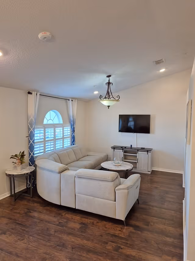 Bright living room featuring a light gray sectional, round coffee table, wall-mounted TV, and arched window.