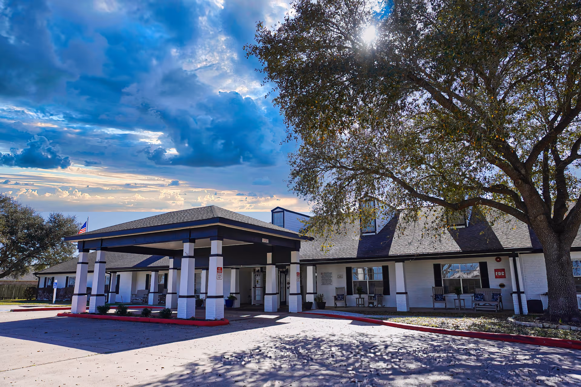 Front exterior of Sodalis Victoria Assisted Living with entrance canopy, parking, and a large tree.