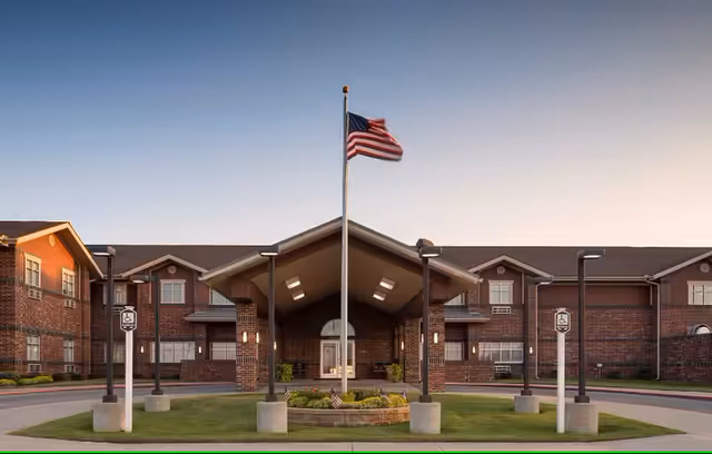 Front view of Autumn Lane Personal Care building with brick facade, porte-cochère, flagpole, and landscaping.