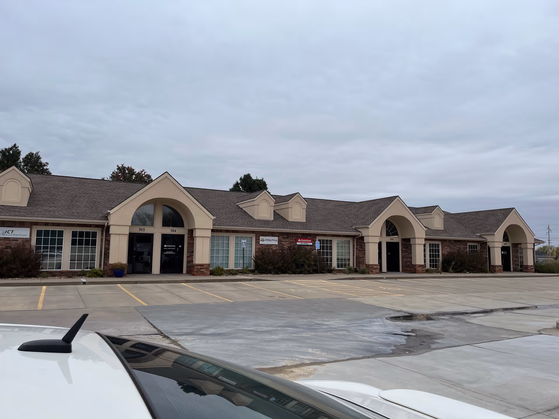 Exterior of a one-story building with arched entryways and a large parking lot.