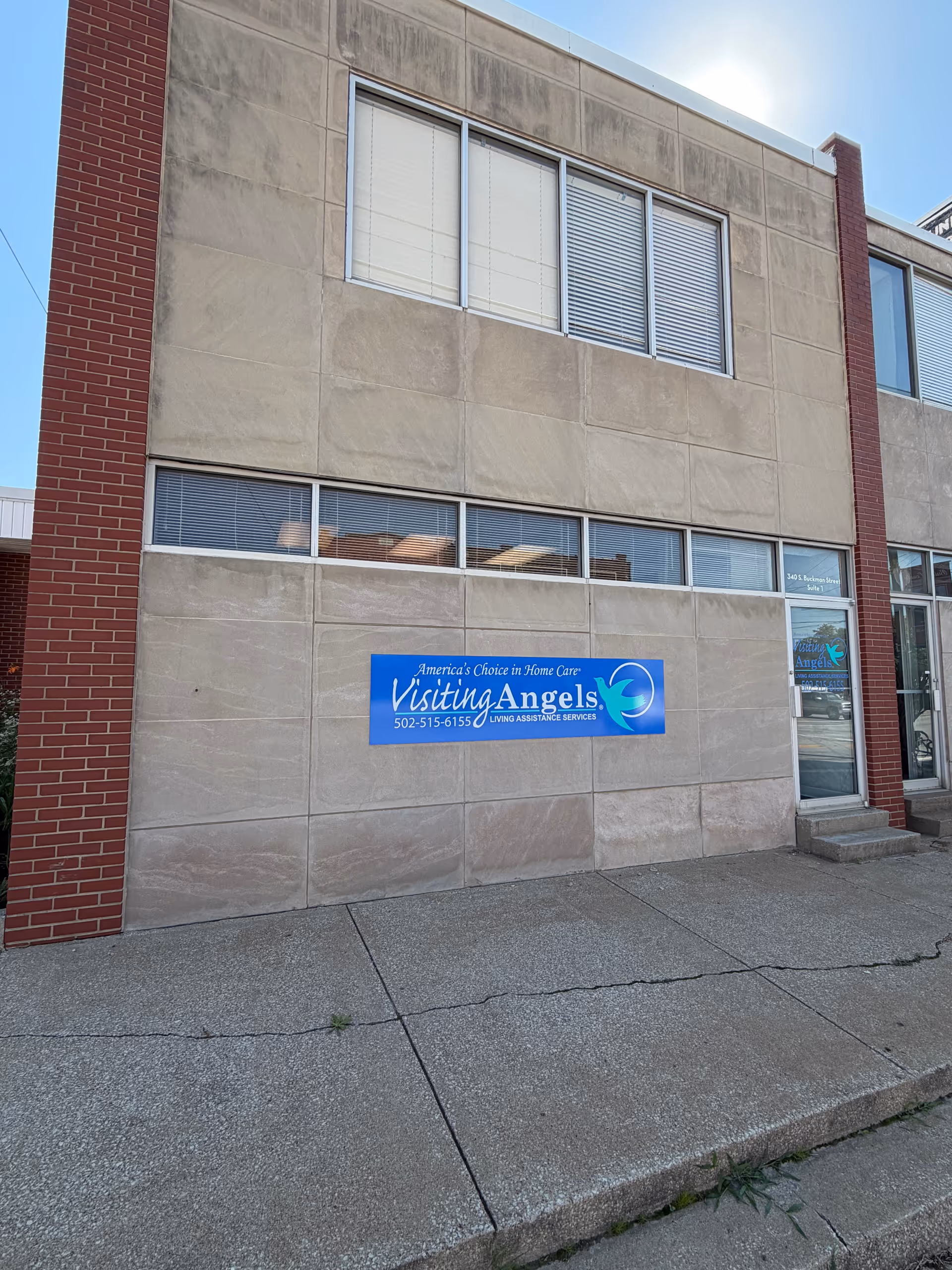 Exterior view of a beige Visiting Angels building with a blue sign and entrance door.