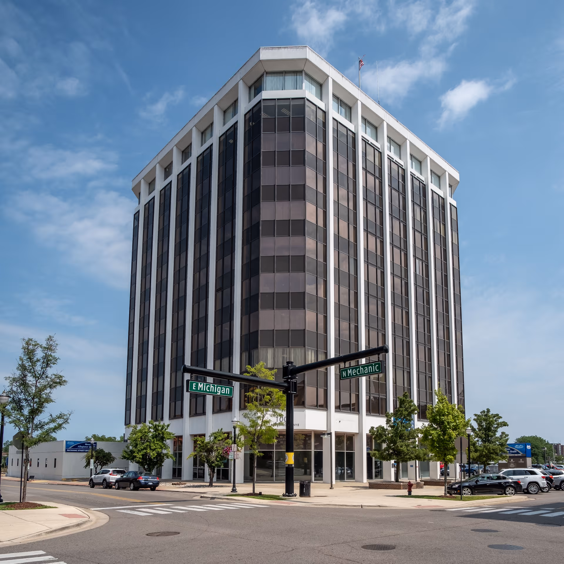 A tall modern office-style building sits at a street corner against a blue sky.