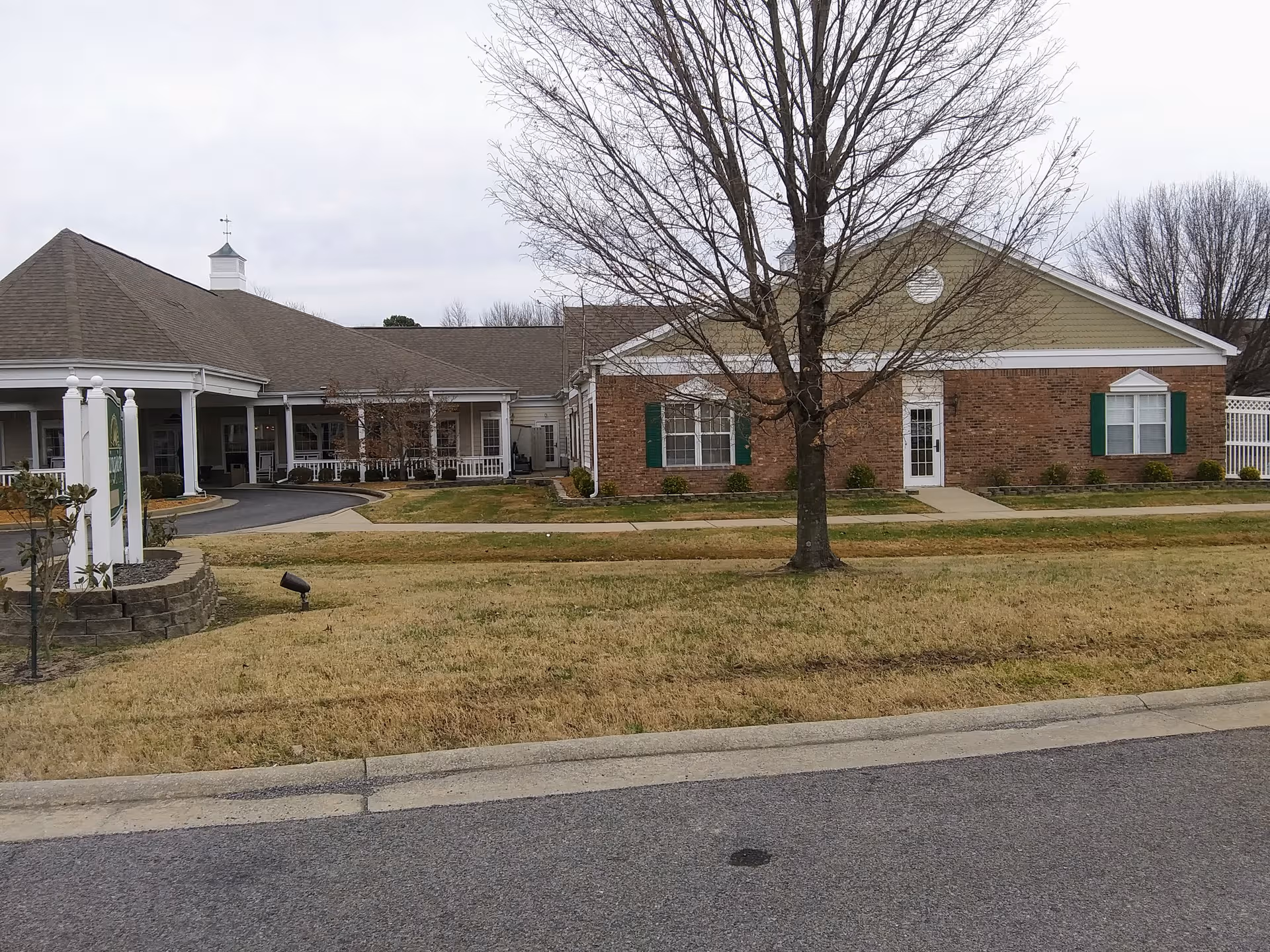 Brick senior living facility with green shutters, white doors, and a leafless tree in front yard.