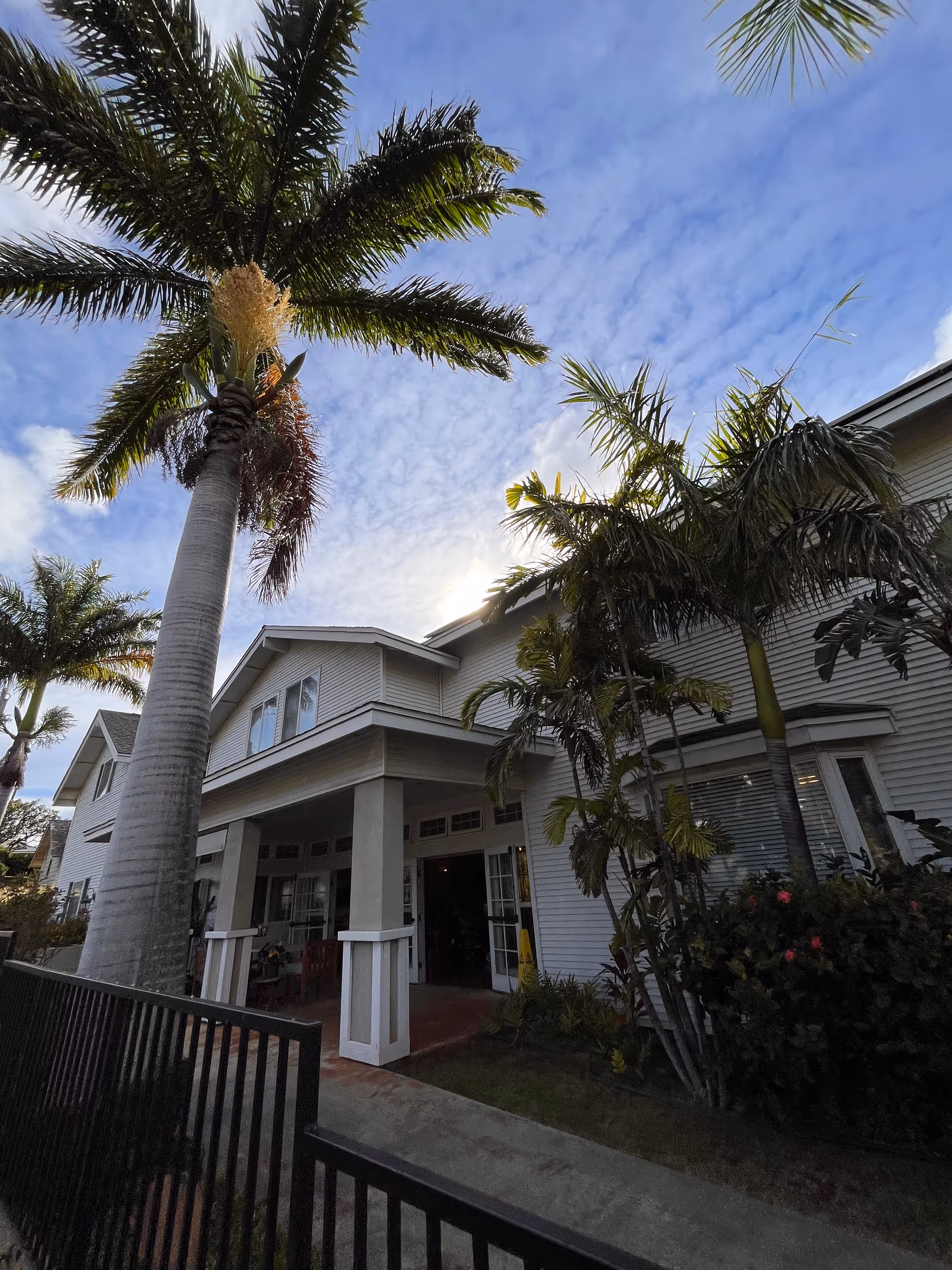 White senior care facility exterior with a covered entrance and palm trees