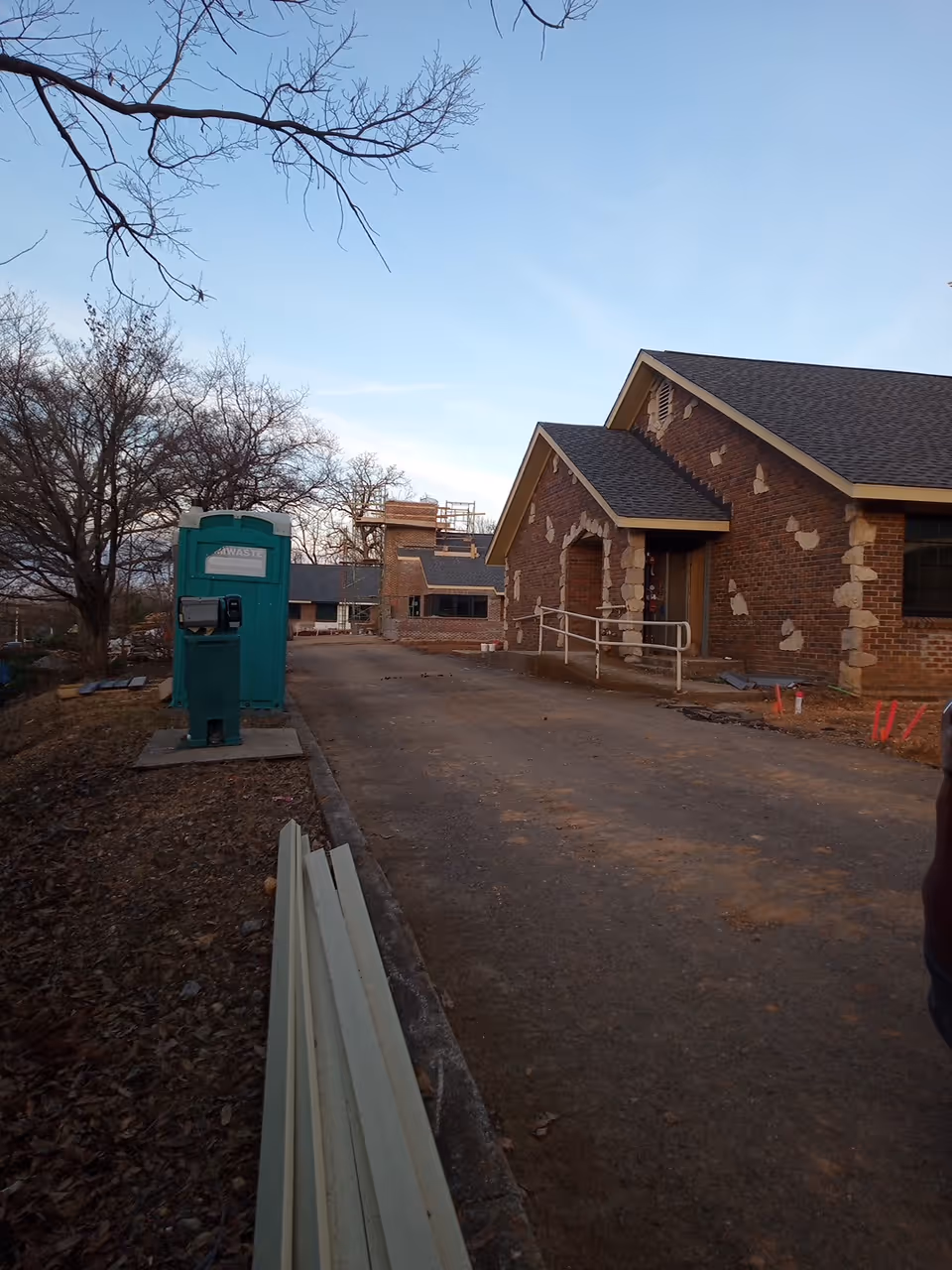 Front exterior of a brick building under construction with a portable toilet nearby